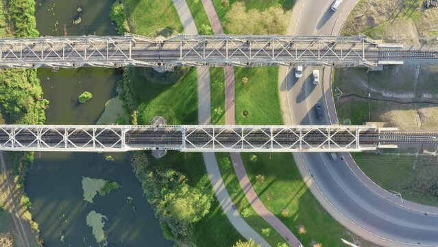Top aerial view of railway bridges over the river and bendy road with moving cars.