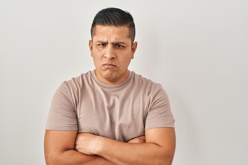 Hispanic young man standing over white background skeptic and nervous, disapproving expression on face with crossed arms. negative person.