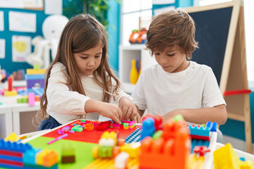 Brother and sister playing with construction blocks sitting on table at kindergarten