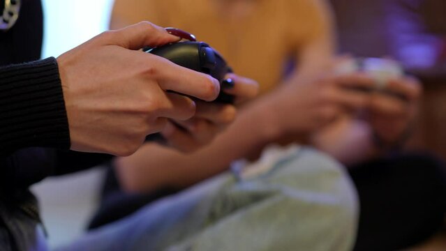 Close-up female hands using joystick moving buttons playing multiplayer video game. Unrecognizable slim young woman sitting indoors gaming with blurred friend side view