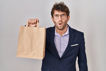 Hispanic business man holding delivery bag scared and amazed with open mouth for surprise, disbelief face