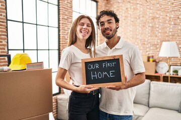 Young two people holding blackboard with first home text sticking tongue out happy with funny expression.