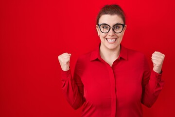 Young hispanic woman with red hair standing over red background celebrating surprised and amazed for success with arms raised and open eyes. winner concept.