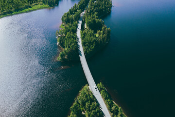 Aerial view of road over blue lake water and green woods in Finland.