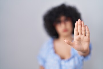 Young brunette woman with curly hair wearing glasses over isolated background doing stop sing with...