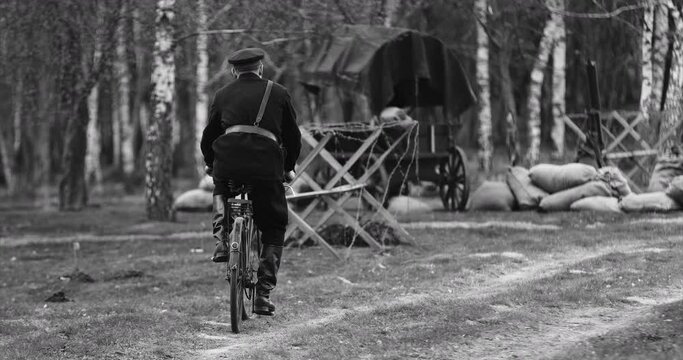 Re-enactor Dressed As Nkvd Forces Rides A Bike. Peoples Commissariat For Internal Affairs, Abbreviated Nkvd, Was Interior Ministry Of The Soviet Union. Black And White Video.