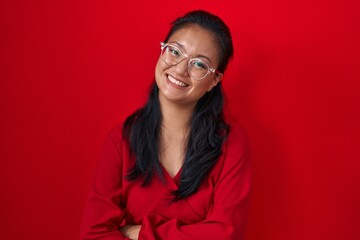 Asian young woman standing over red background happy face smiling with crossed arms looking at the camera. positive person.