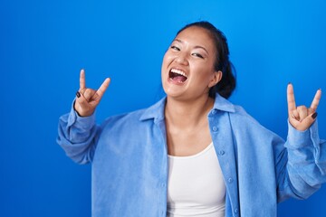 Asian young woman standing over blue background shouting with crazy expression doing rock symbol with hands up. music star. heavy music concept.