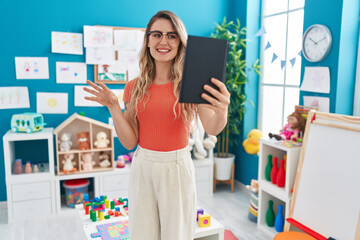 Young blonde woman teacher having video call standing at kindergarten