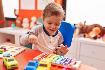 Adorable caucasian boy playing xylophone sitting on table at kindergarten