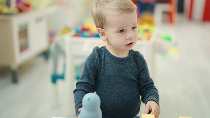 Adorable blond toddler standing with relaxed expression at kindergarten