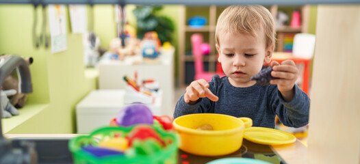 Adorable blond toddler playing with play kitchen standing at kindergarten