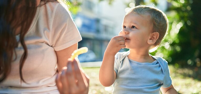 Mother And Son Sitting On Bench Together Eating Little Worms Snack At Park