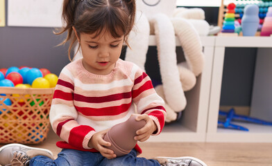 Adorable hispanic girl playing with toys sitting on floor at kindergarten