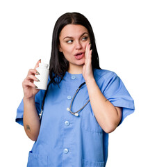 Young nurse woman holding pills isolated is saying a secret hot braking news and looking aside