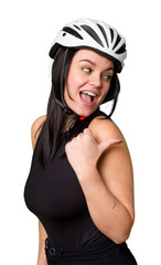 Young caucasian woman wearing a helemet isolated points with thumb finger away, laughing and carefree.