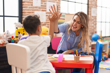 Teacher and toddler sitting on table high five at kindergarten