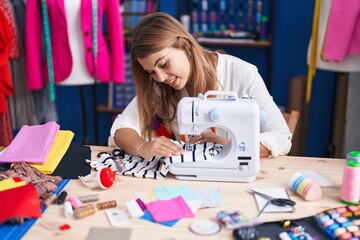 Fototapeta premium Young woman tailor smiling confident using sewing machine at sewing studio