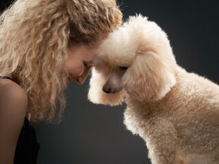 happy girl with a dog in a photo studio on black. white Poodle and curly woman