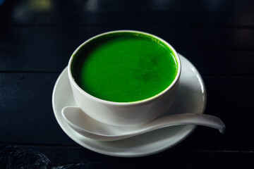 Green spinach soup in a white plate on a dark background. Healthy food for vegetarians. Copy space