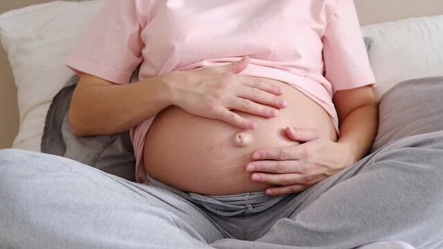 Young pregnant woman in home clothes strokes her big belly