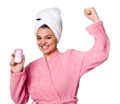 A woman, dressed in a cozy pink bathrobe and a towel on her head, holds a deodorant with a big smile. Enjoying the comfort of her spa-like routine