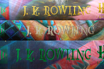 Fototapeta premium Split, Croatia - January 15, 2023: Stack of fantasy books by famous author J. K. Rowling. Bookshelf in the background. Selective focus.