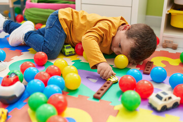 Fototapeta na wymiar Adorable caucasian boy playing with car toy lying on floor at kindergarten