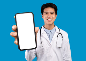 Online Medicine. Smiling Asian Doctor Man Showing Big Blank Smartphone At Camera