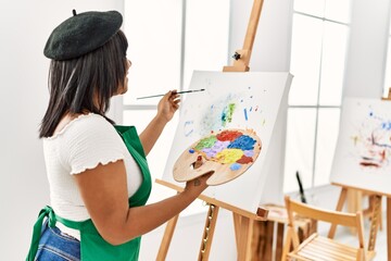 Hispanic brunette woman painting on canvas at art studio