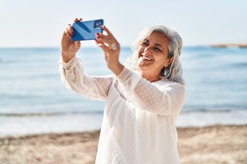 Middle age woman smiling confident making selfie by the smartphone at seaside