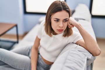 Young beautiful hispanic woman sitting on sofa with serious expression at home