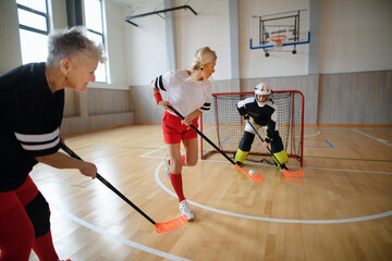 Multigenerational woman floorball team playing together in a gym.