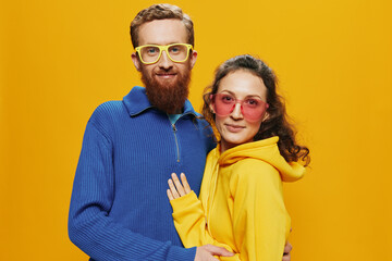Fototapeta premium Man and woman couple smiling cheerfully and crooked with glasses, on yellow background, symbols signs and hand gestures, family shoot, newlyweds.