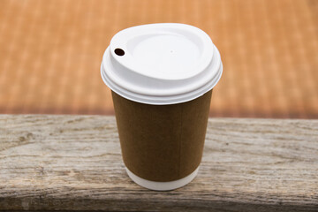 Terracotta paper cup with coffee on the wooden railing of the stairs in the park