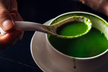 A person has a cream of spinach soup. Close-up of a hand holding a spoon over a plate. Ordinary life