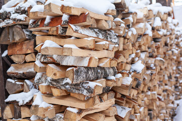 Stacked firewood covered with white snow, wood for kindling and heating. woodpile with stacked firewood birch tree covered fresh icy frozen snow and snowflakes. cold weather and snowy winter