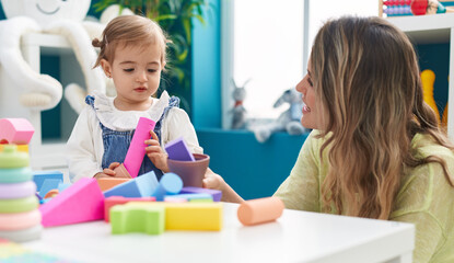 Teacher and toddler playing with geometry blocks sitting on table at kindergarten
