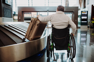 Rear view of man on wheelchair at airport with his luggage.