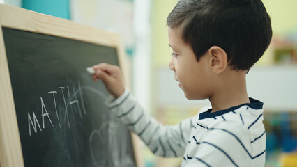 Adorable hispanic boy preschool student writing on blackboard at kindergarten