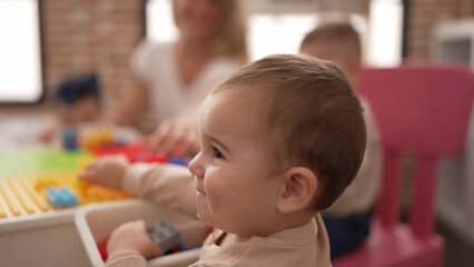 Adorable toddler holding plastic construction blocks sitting on table at kindergarten