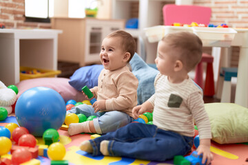 Two adorable toddlers playing with balls sitting on floor at kindergarten