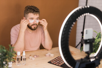 Male beauty blogger doing his make up and recording a video lesson his with mobile phone - vlog, diversity and video blog concept