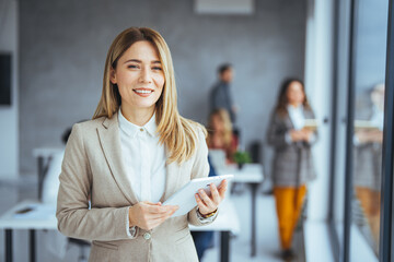 Young attractive female manager working on digital tablet while standing in modern office. Confident business expert. 