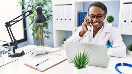 African american woman doctor using laptop talking on telephone at clinic