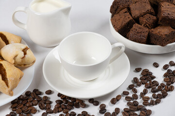 Empty coffee ceramic cup with milk jug, chocolate cake and coffee beans on a white background
