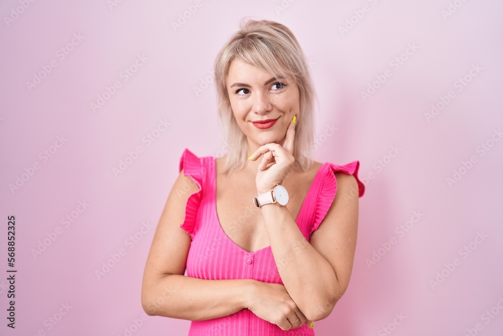 Poster Young caucasian woman standing over pink background with hand on chin thinking about question, pensive expression. smiling and thoughtful face. doubt concept.