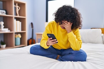 Young beautiful hispanic woman using smartphone with worried expression at bedroom