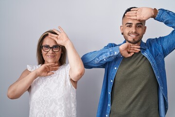 Hispanic mother and son standing together smiling cheerful playing peek a boo with hands showing...
