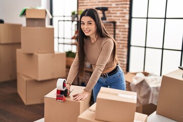 Young beautiful hispanic woman smiling confident packing cardboard box at new home